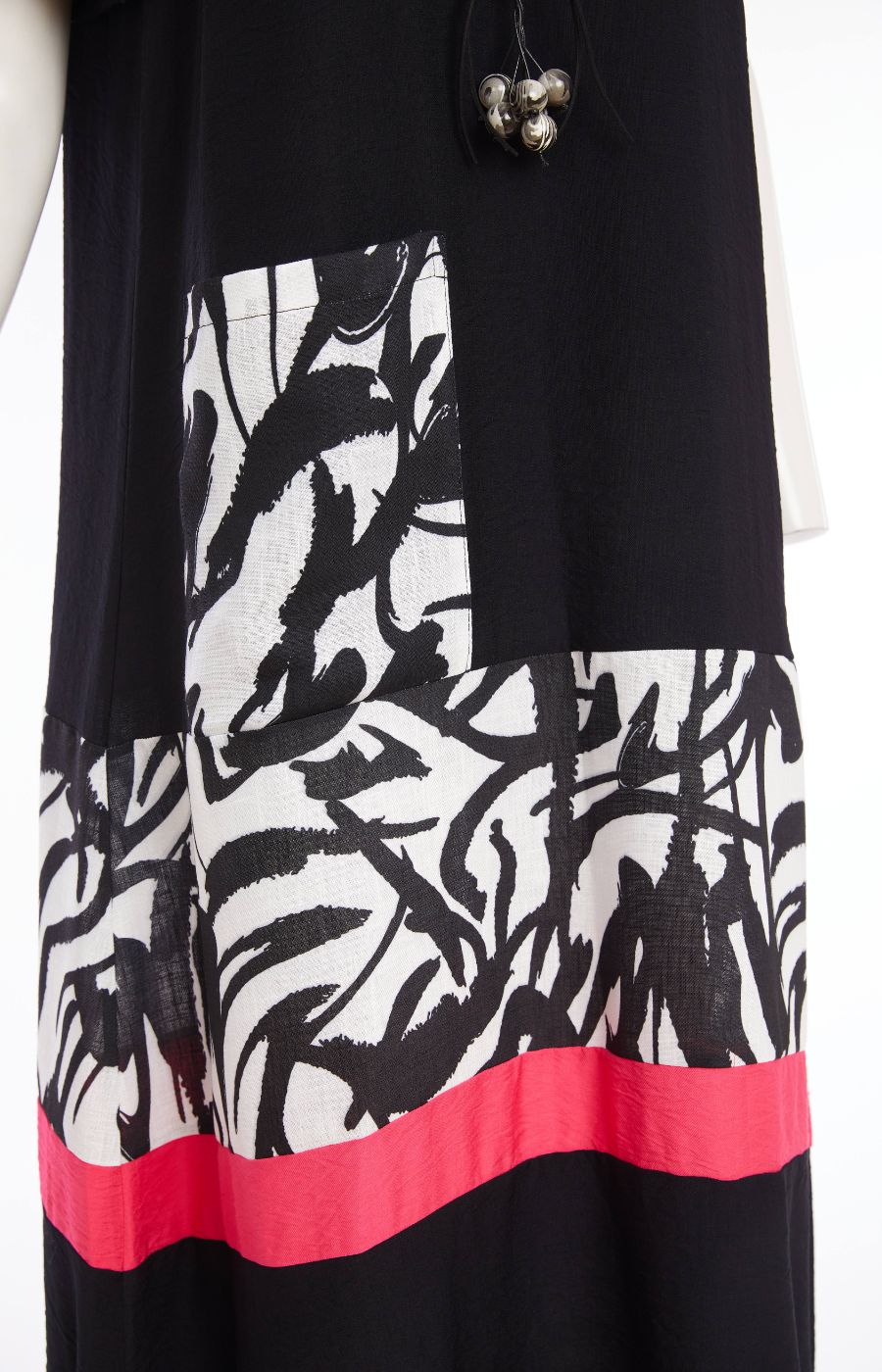 Woman wearing the Ora Dress in Black with Necklace, a black dress with a white, black and pink  design on the fron, front pocket, short sleeves and a round neckline against a white background 