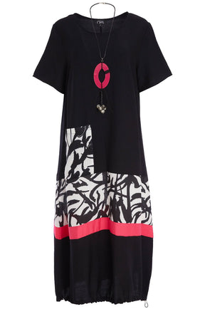 Woman wearing the Ora Dress in Black with Necklace, a black dress with a white, black and pink  design on the fron, front pocket, short sleeves and a round neckline against a white background 
