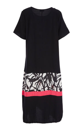 Woman wearing the Ora Dress in Black with Necklace, a black dress with a white, black and pink  design on the fron, front pocket, short sleeves and a round neckline against a white background 