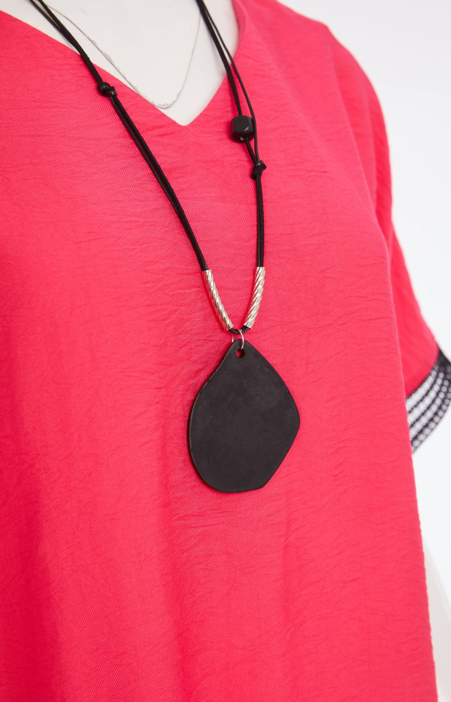 Woman wearing the Ora Feather Print Top in Pink, a pink blouse with black trim, front pocket,  V neckline and short sleeves and black trousers against a white background, Necklace in this picture included