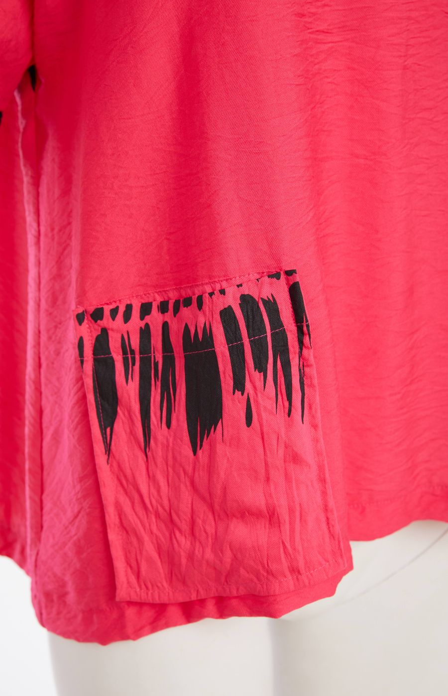 Woman wearing the Ora Feather Print Top in Pink, a pink blouse with black trim, front pocket with feather print,  V neckline and short sleeves and black trousers against a white background