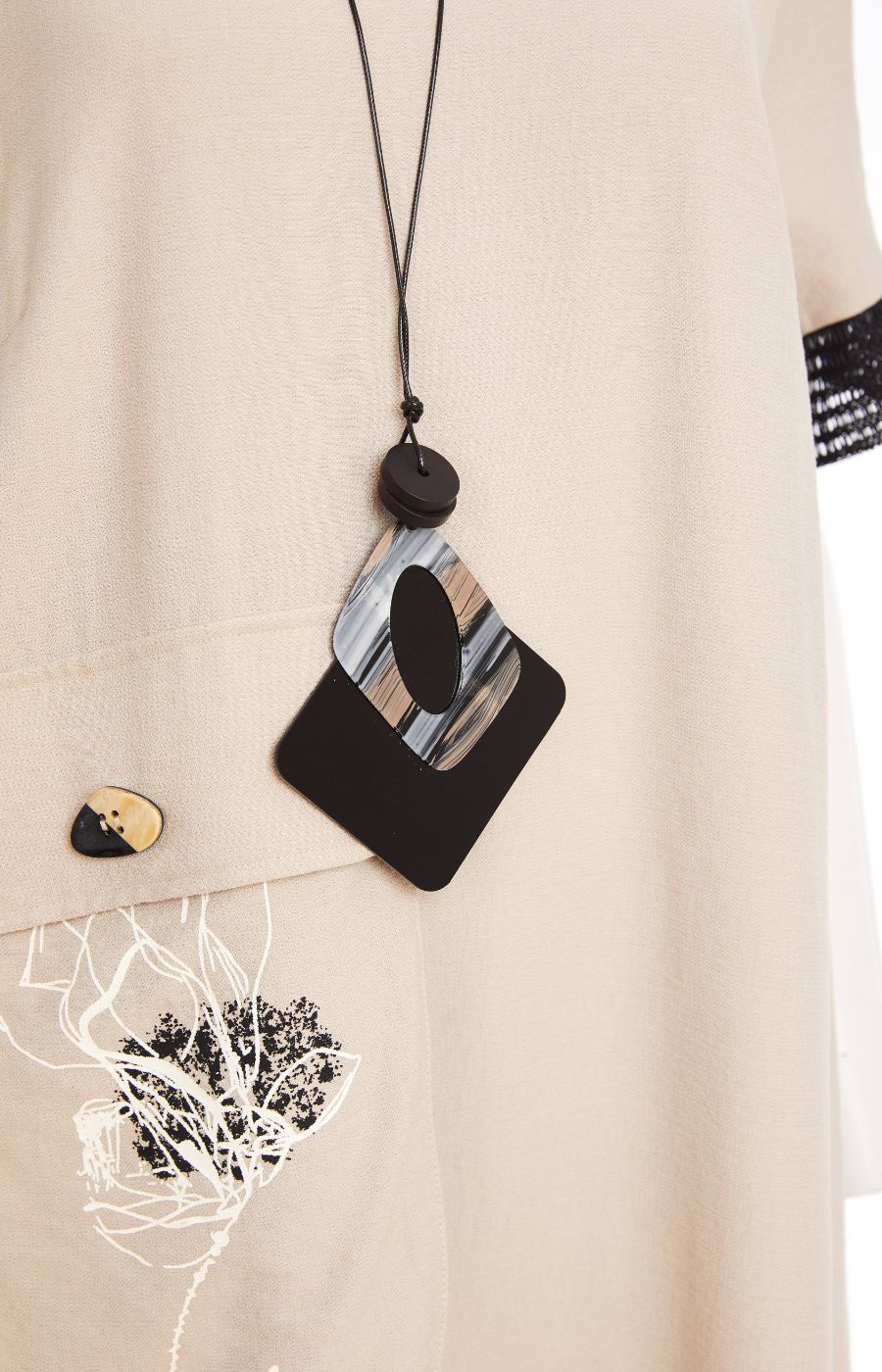 Woman wearing the Ora Front Pocket Dress in Beige, a beige midi dress with black mesh accents on the cuffs of the short sleeves and side slits, has a round neckline, large front pocket, discreet side pockets and necklace included in a minimal indoor setting 