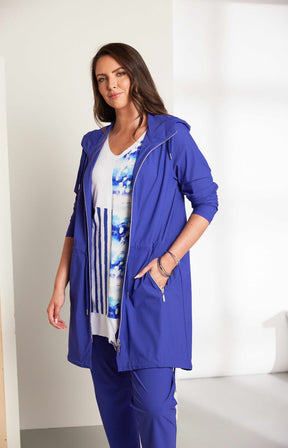 Woman wearing the Ora Hooded Jacket in Blue, with the blue Ora travel trousers a blue outfit with a white background