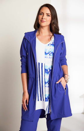 Woman wearing the Ora Hooded Jacket in Blue, with the blue Ora travel trousers a blue outfit with a white background 
