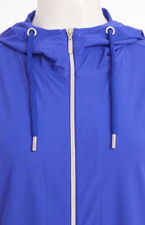 Woman wearing the Ora Hooded Jacket in Blue, with the blue Ora travel trousers a blue outfit with a white background  