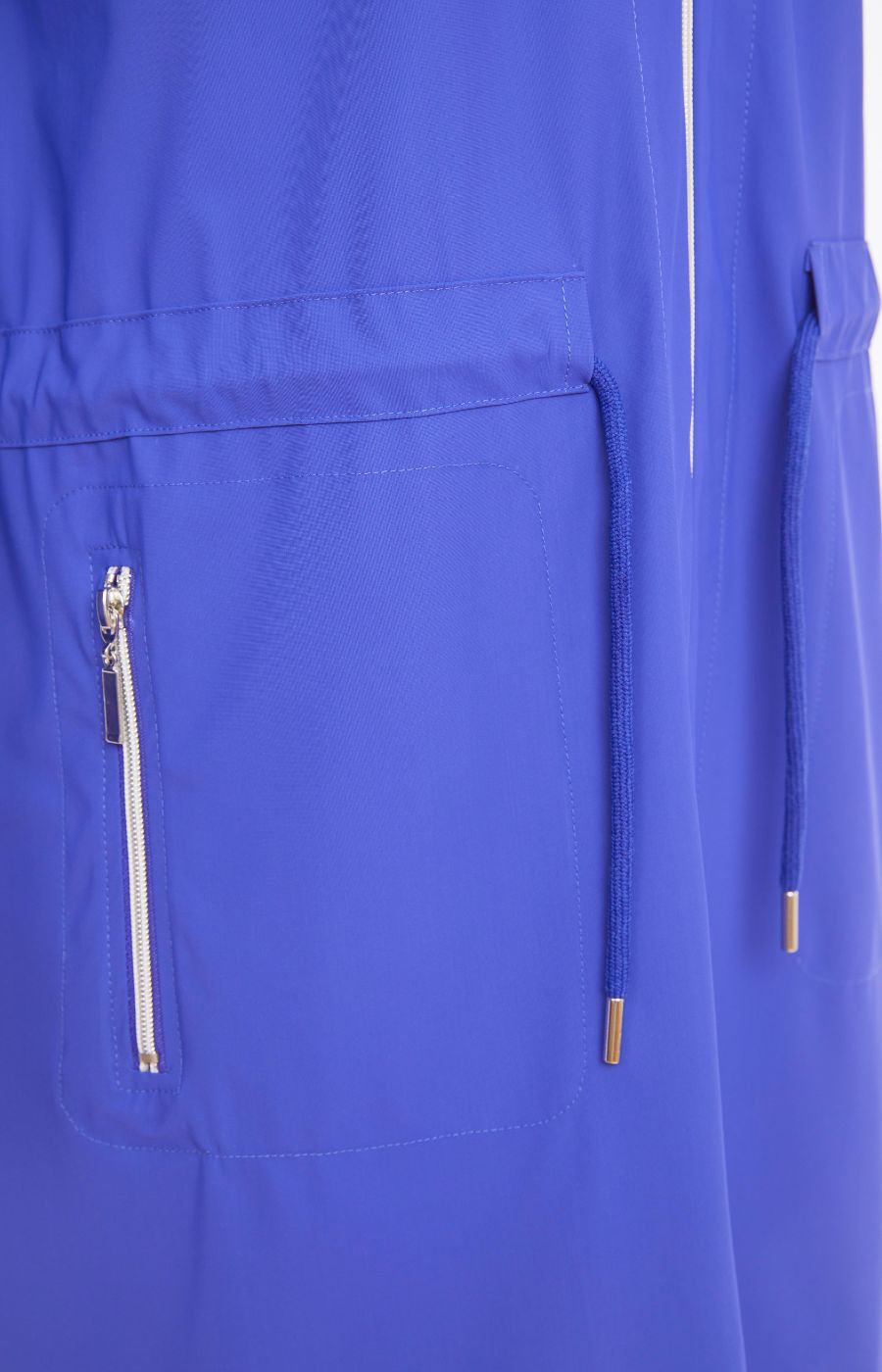 Woman wearing the Ora Hooded Jacket in Blue, with the blue Ora travel trousers a blue outfit with a white background  