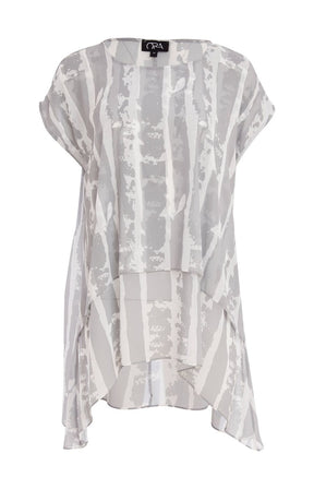 Woman wearing the Ora Layered Top in Grey, a slightly sheer, double layered top with a  light grey and white patterned top. Has a round neckline, short sleeves and a curved hem worn with white trousers against a plain background   
