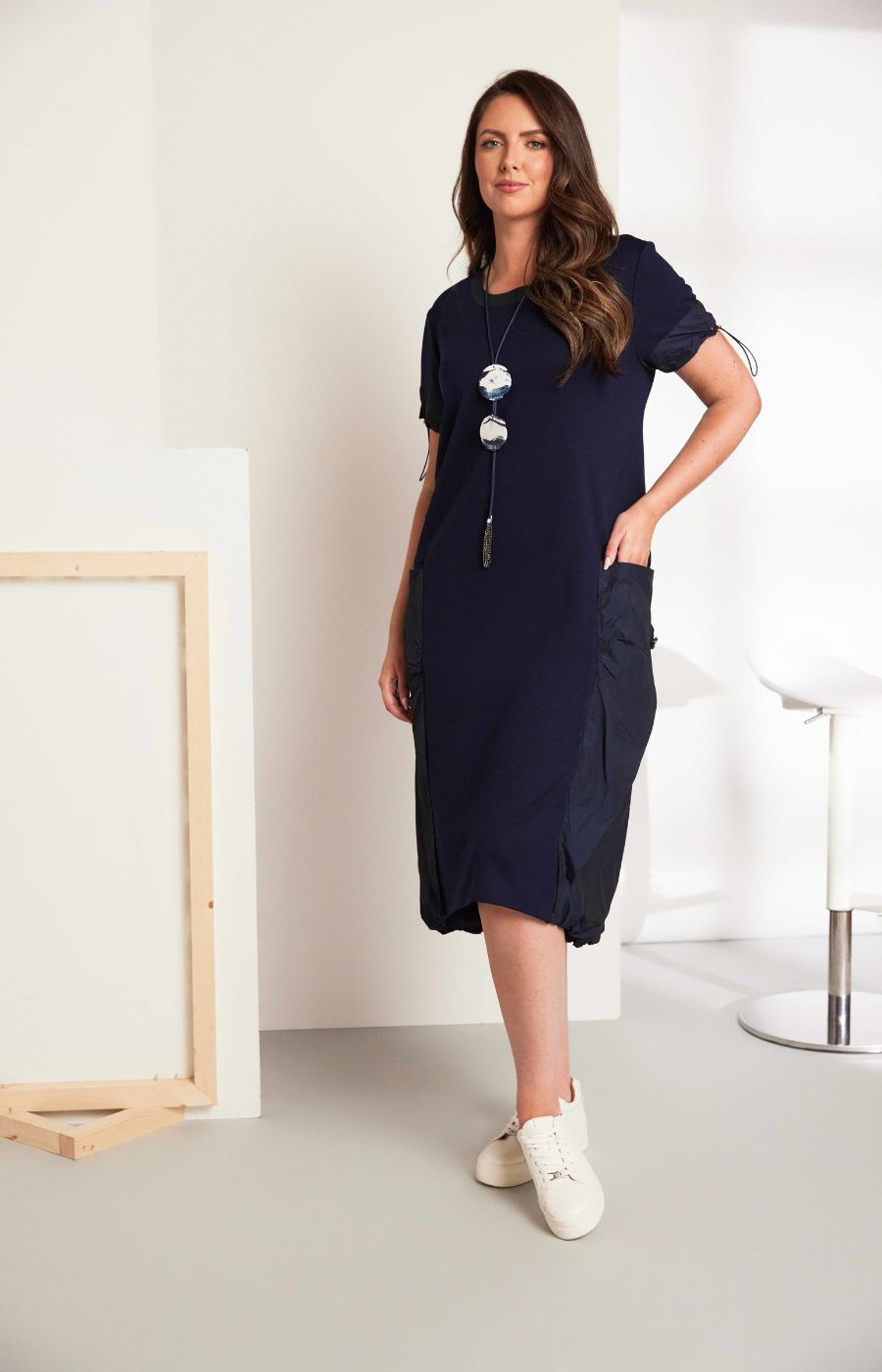 Woman wearing the Ora Side Pocket Dress in Navy, a navy blue dress with side pockets, round neckline and short sleeves, in a midi length.