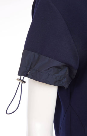 Woman wearing the Ora Side Pocket Dress in Navy, a navy blue dress with side pockets, round neckline and short sleeves, in a midi length. 