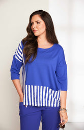 Woman wearing the Ora Striped Pocket Top in Blue, a blue top a round neckline and 3/4 length sleeves with white striped hem against a plain background