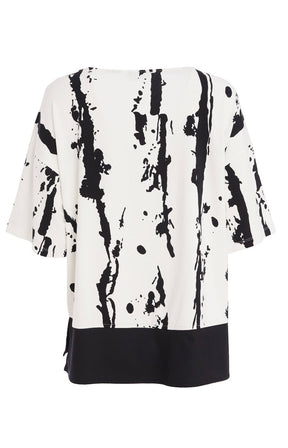 Woman wearing the Ora White and Black Stripe Top, a black and white messy stripe patterned top with 1/2 length sleeves, round neckline, relaxed fit and contrasting hem worn with black trousers.