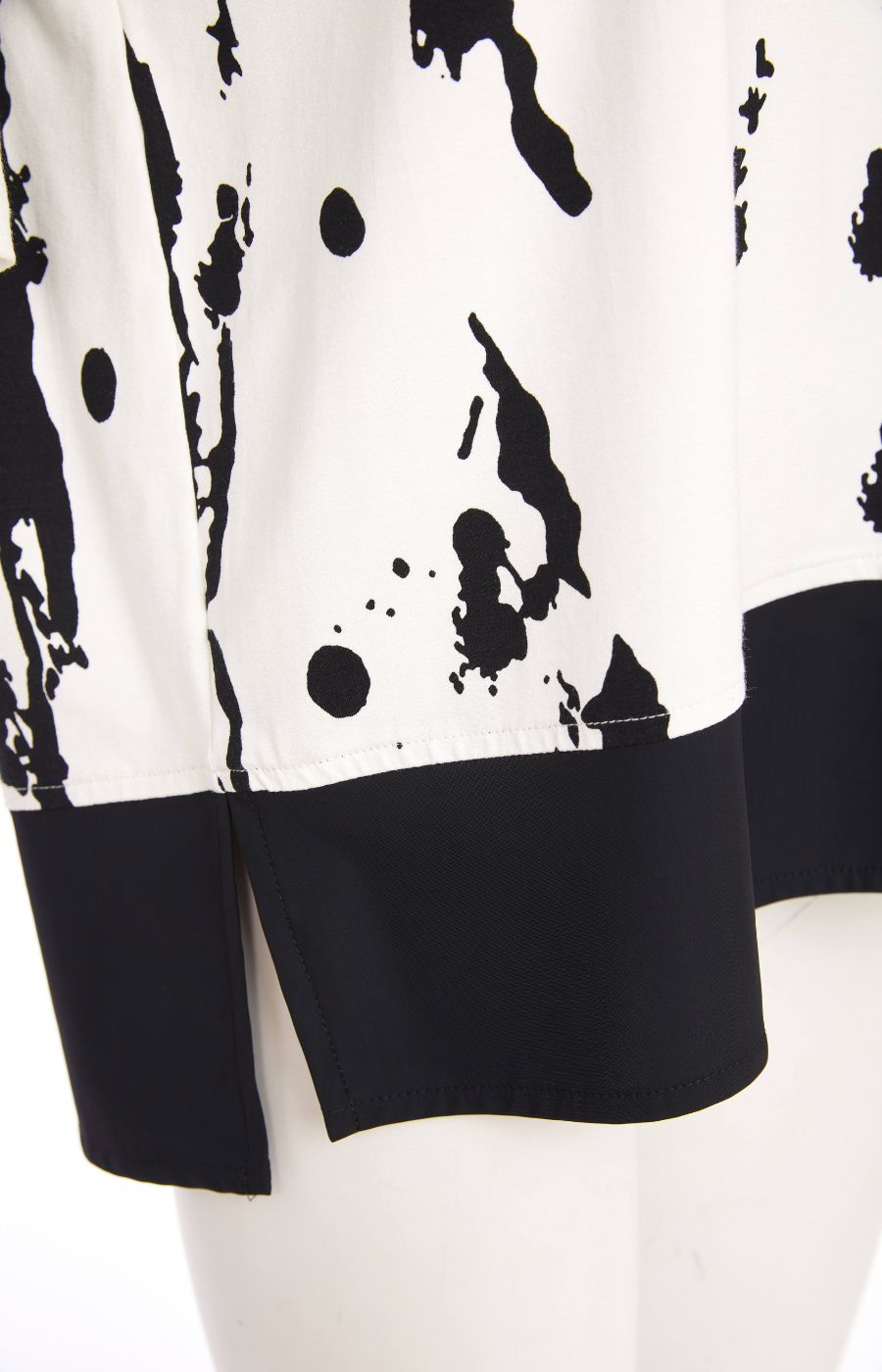 Woman wearing the Ora White and Black Stripe Top, a black and white messy stripe patterned top with 1/2 length sleeves, round neckline, relaxed fit and contrasting hem with side slits worn with black trousers. 