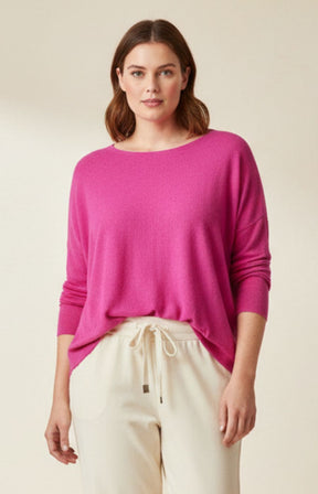 Woman wearing a bright pink sweater and beige pants on a plain background