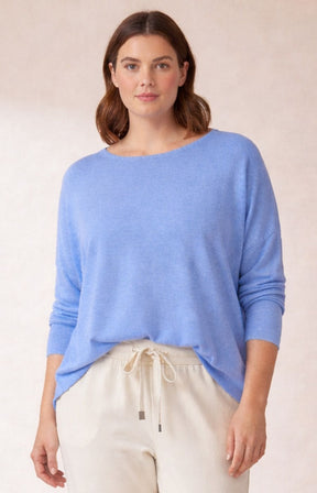 Woman wearing a blue sweater and beige pants on a plain background