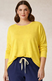 Woman wearing a yellow knit sweater and navy pants on a plain background