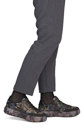 A close-up of a person's legs wearing dark gray trousers, black socks, and low-top sneakers with a dark camouflage pattern on the uppers and soles.