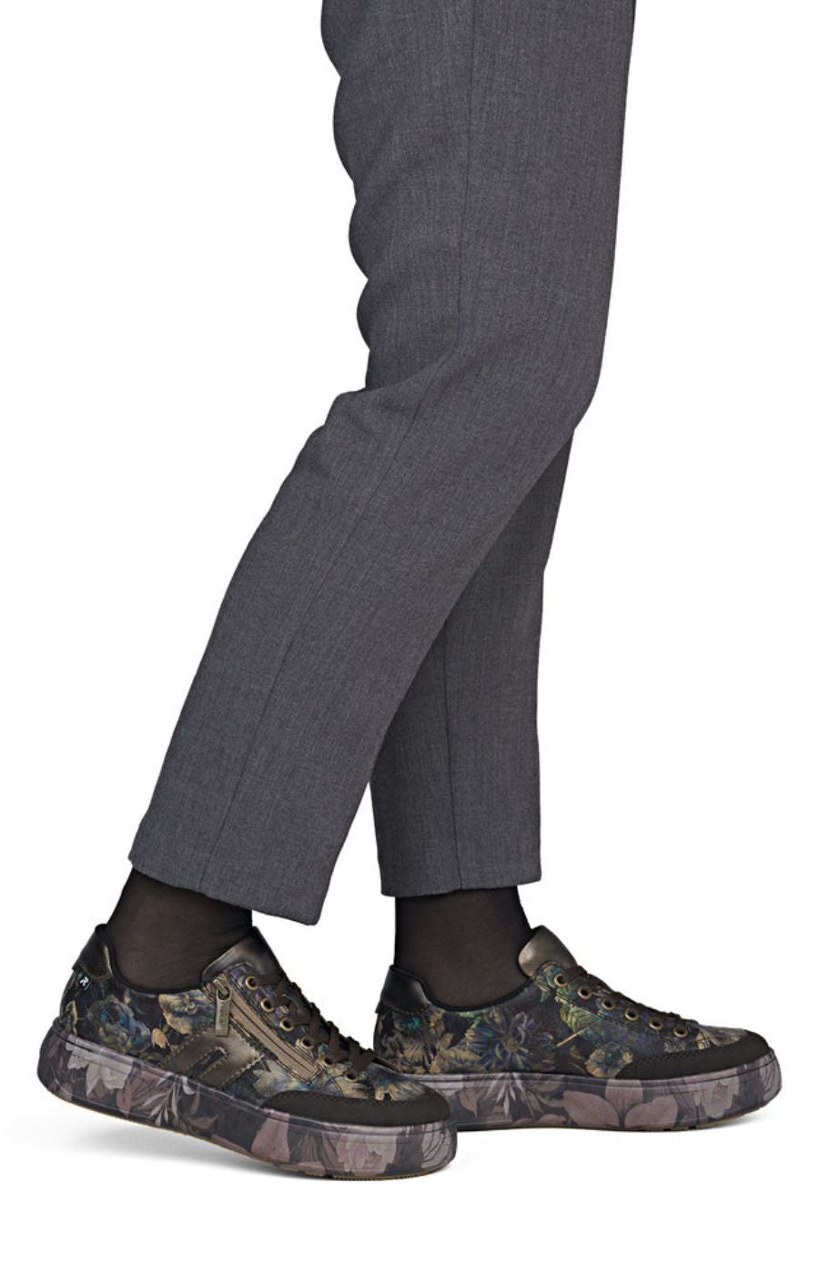 A close-up of a person's legs wearing dark gray trousers, black socks, and low-top sneakers with a dark camouflage pattern on the uppers and soles.
