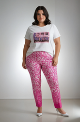 Woman wearing a white t-shirt with a graphic design and pink patterned trouser on a plain background