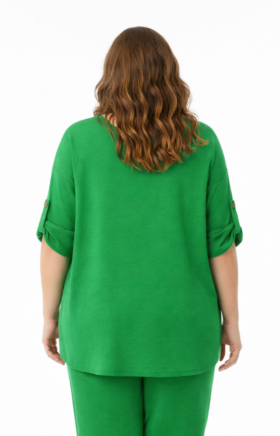 A woman standing against a plain white background wearing a green blouse with rolled-up sleeves, paired with matching green cropped pants. 