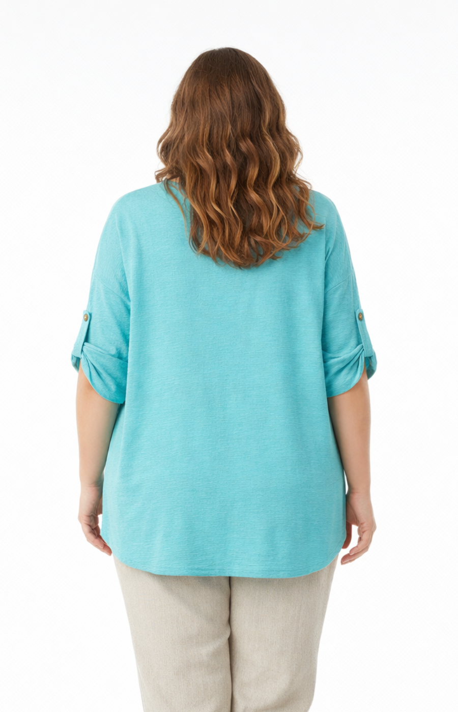 A woman standing against a plain white background wearing a mint blouse with rolled-up sleeves, paired with beige pants. She is barefoot