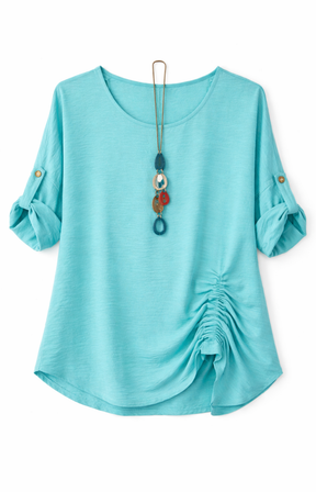 Mint blouse with rolled-up sleeves and a gathered detail on one side, accessorized with a long, colorful pendant necklace on a white background