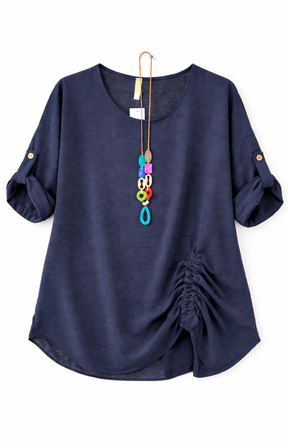 Navy blouse with rolled-up sleeves and a gathered detail on one side, accessorized with a long, colorful pendant necklace.