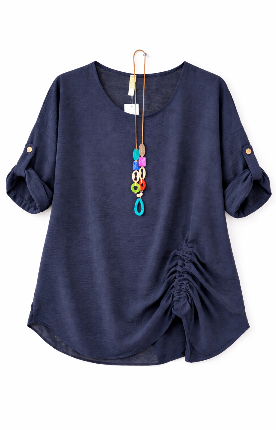 Navy blouse with rolled-up sleeves and a gathered detail on one side, accessorized with a long, colorful pendant necklace.