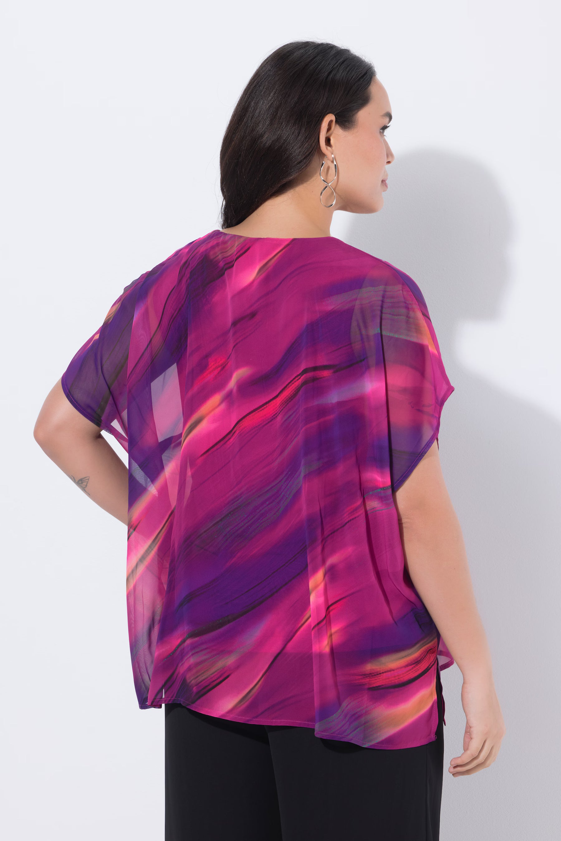 Woman wearing the Ulla Popken Chiffon Blouse in Magenta, a vibrant, abstract-patterned top with a round neckline and short sleeves against a plain background