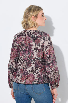A woman shown from the back wearing the Ulla Popken Floral Damask Blouse in Mauve, a long-sleeve floral blouse with a beige base and pink, purple, and black botanical pattern, paired with blue jeans against a light gray studio background.