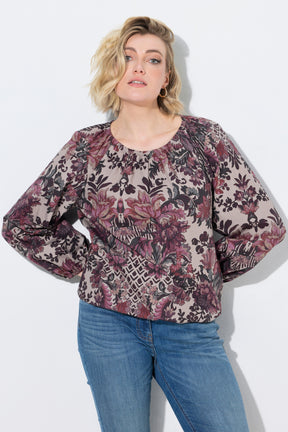 A woman wearing the Ulla Popken Floral Damask Blouse in Mauve, a long-sleeve blouse with a dense floral and botanical pattern in dusty pink, burgundy, and black over a beige base, paired with blue jeans, against a plain white background.