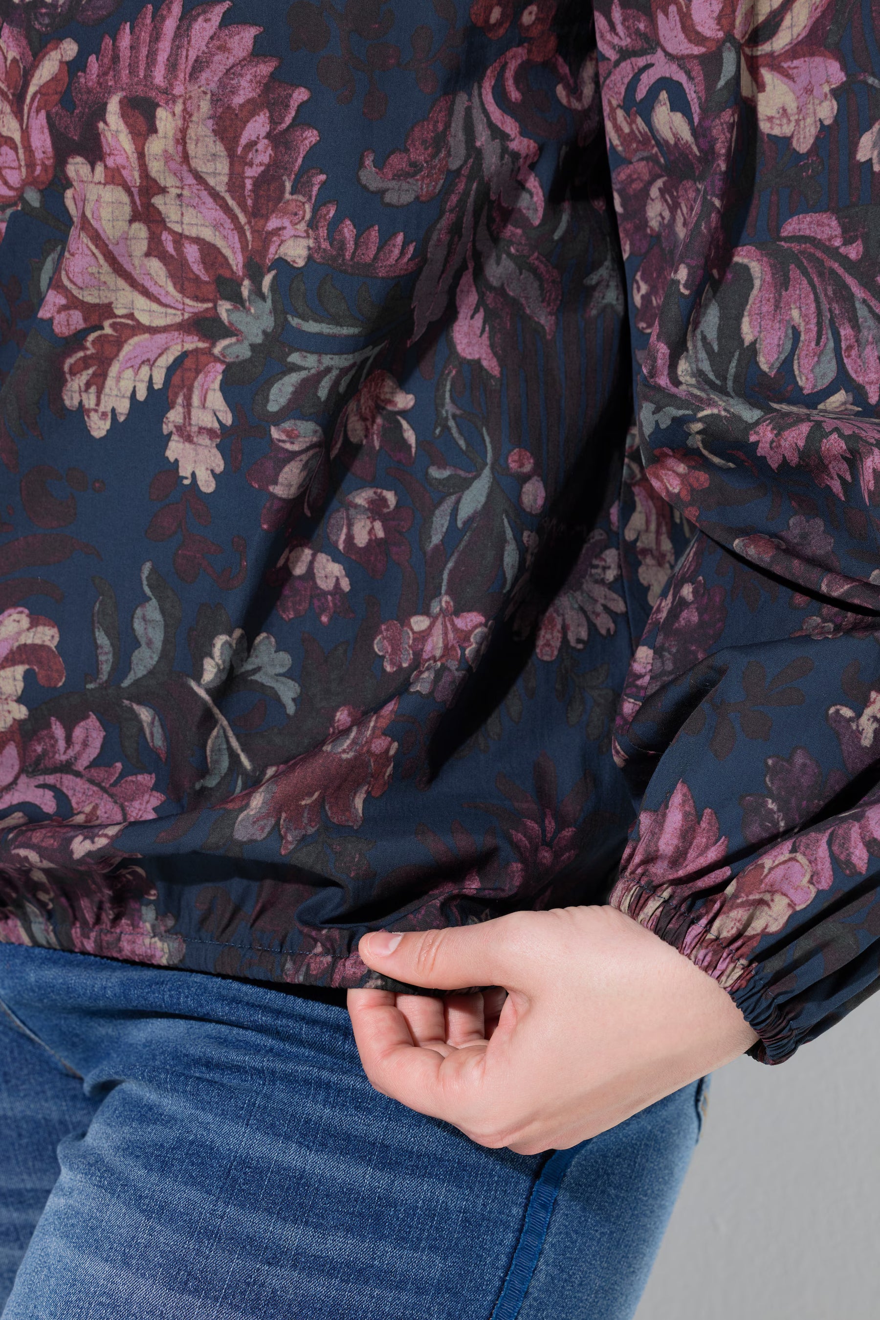 Close-up of a women wearing the Ulla Popken Floral Damask Blouse in Navy, a dark floral jacket with pink and mauve flowers over a navy base, paired with blue jeans.