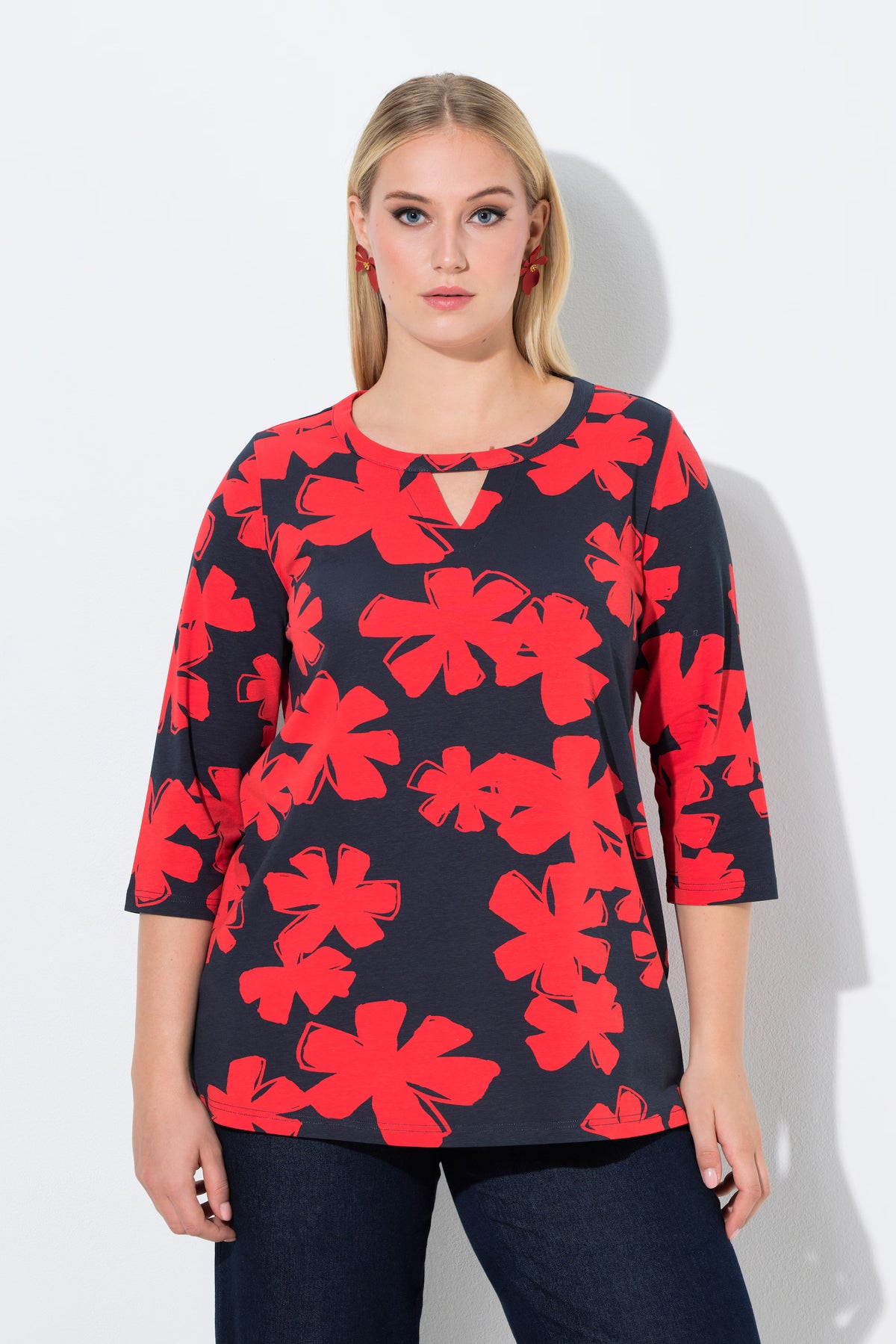 Woman wearing the Ulla Popken Floral Keyhole Top in Red, a navy top with red floral patterns on a white background