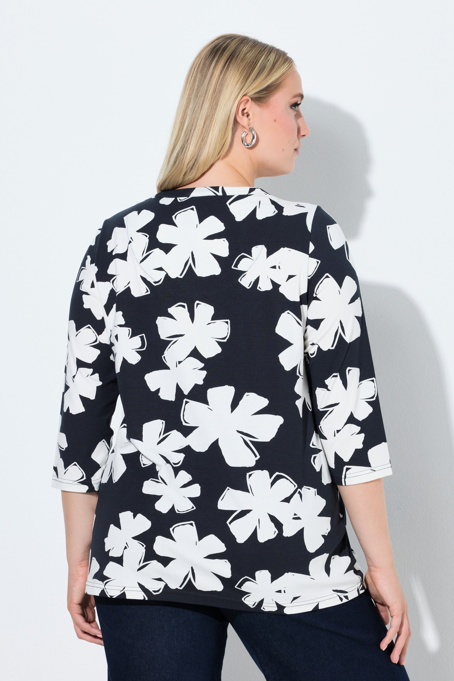 Woman wearing the Ulla Popken Floral Keyhole Top in White, a navy blue top with white floral pattern, a round neckline with a keyhole cut out and 3/4 length sleeves on a plain background
