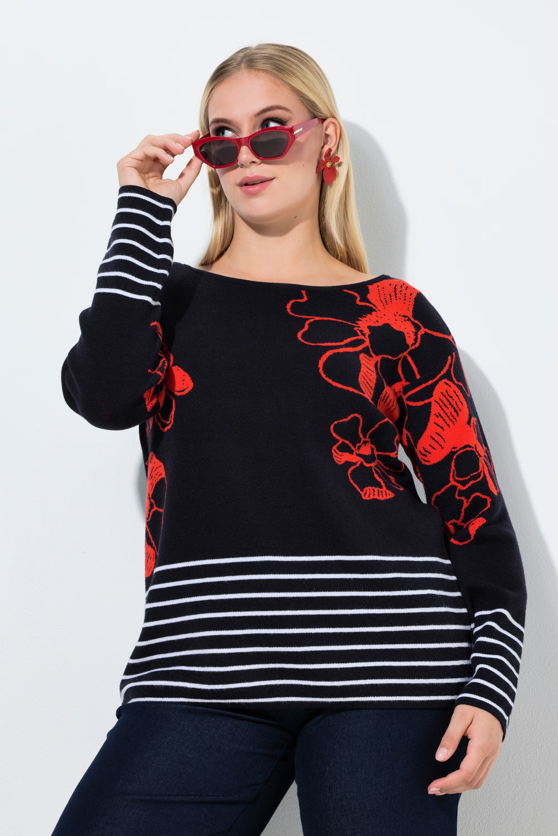 Woman wearing the Ulla Popken Floral Knit Jumper in Black, a black sweater with red floral patterns and white stripes, standing against a white background.