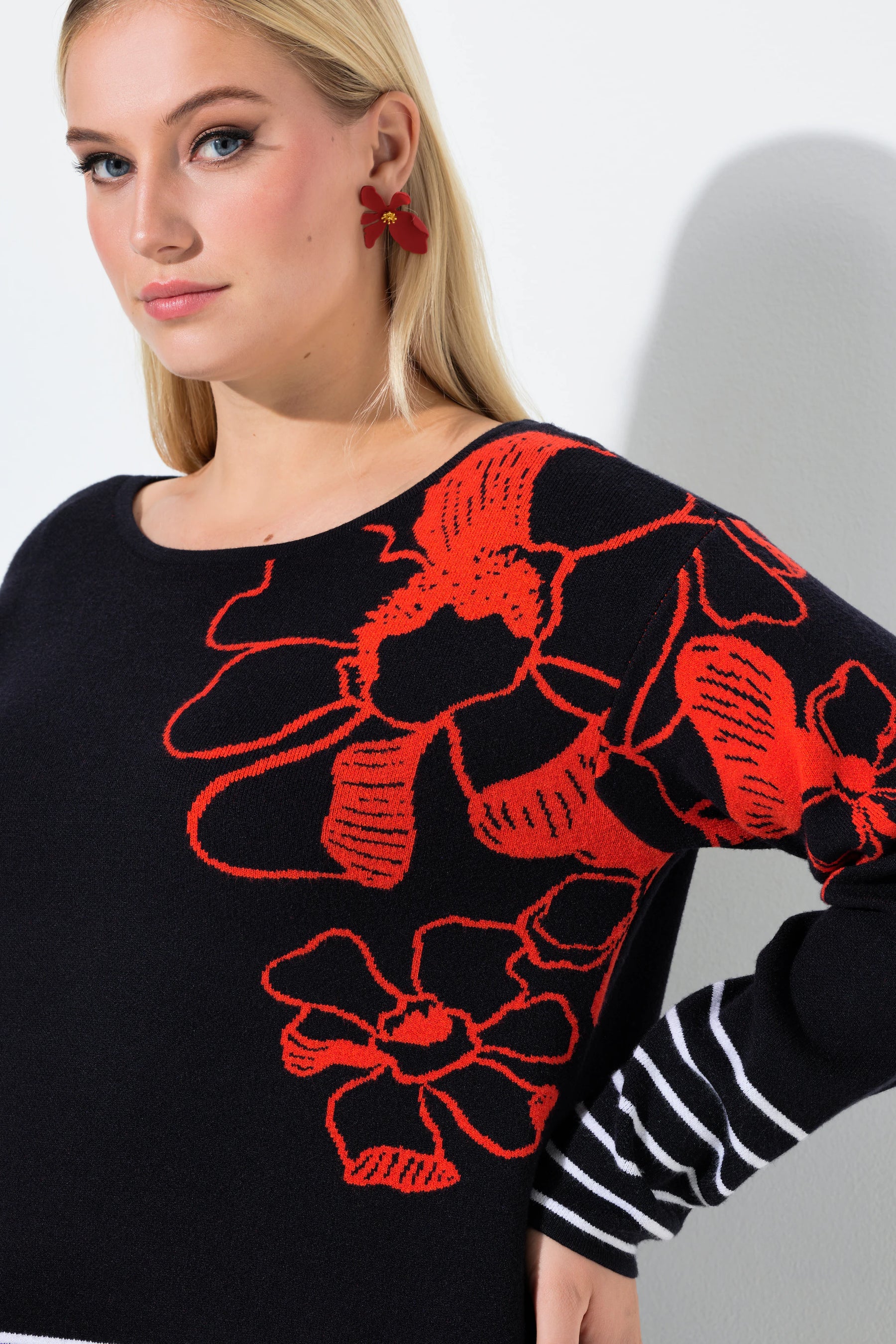 Woman wearing the Ulla Popken Floral Knit Jumper in Black, a black sweater with red floral patterns on a plain background
