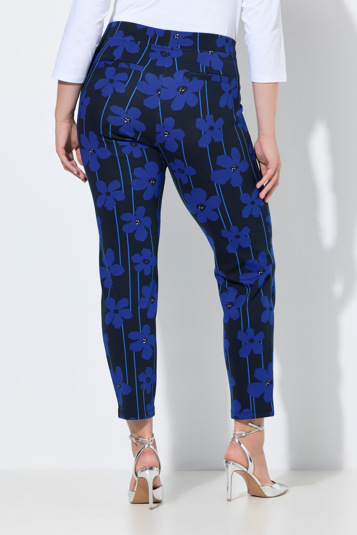 Women wearing the Ulla Popken Floral Trousers in Blue, a dark trousers with a blue floral design all over, has a tapered leg, side pocket  
