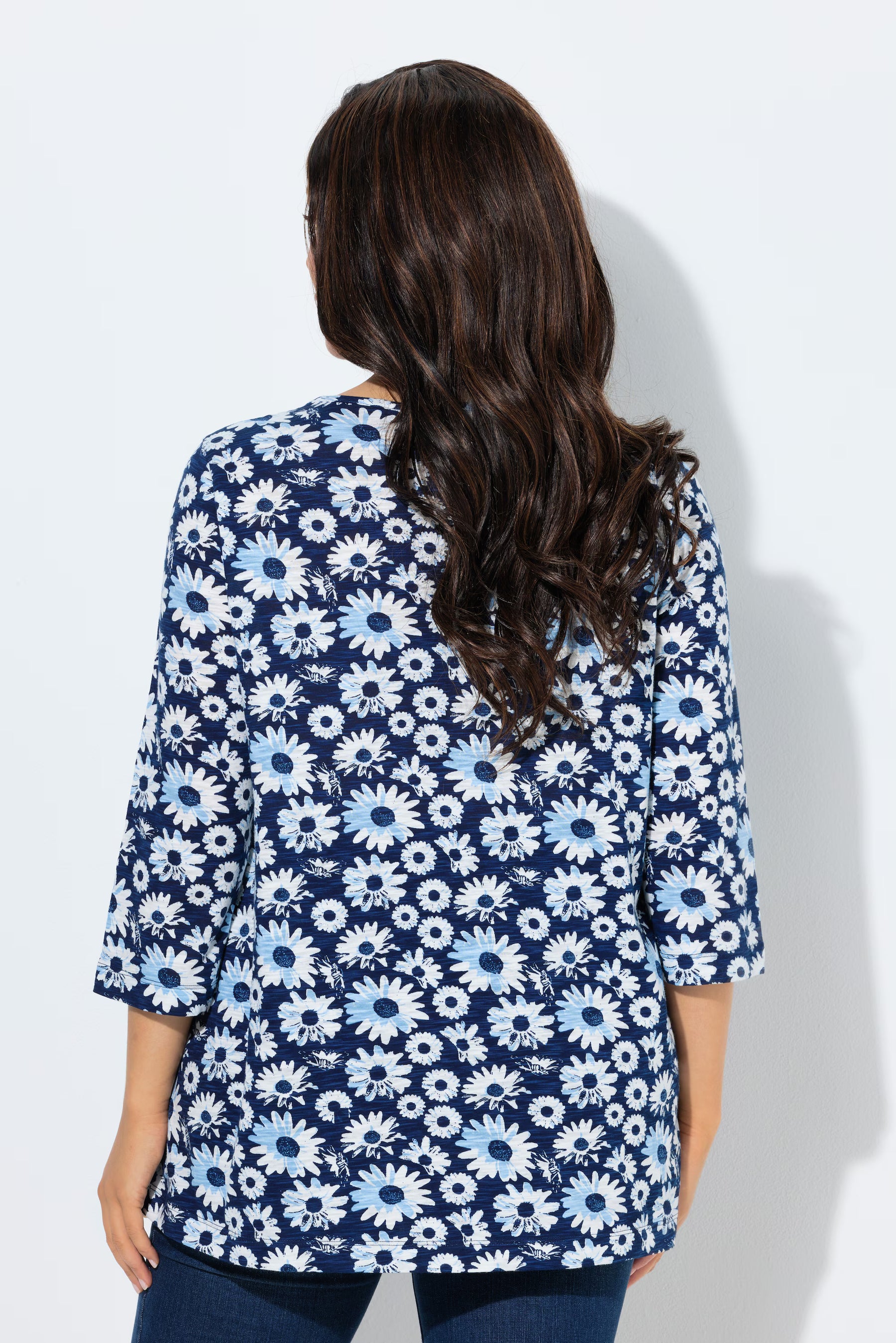 Woman wearing the Ulla Popken Flower Top in Blue, a blue floral patterned top with a V neckline with decorative pleats, 3/4 length sleeves and an A-line shape against a white background
