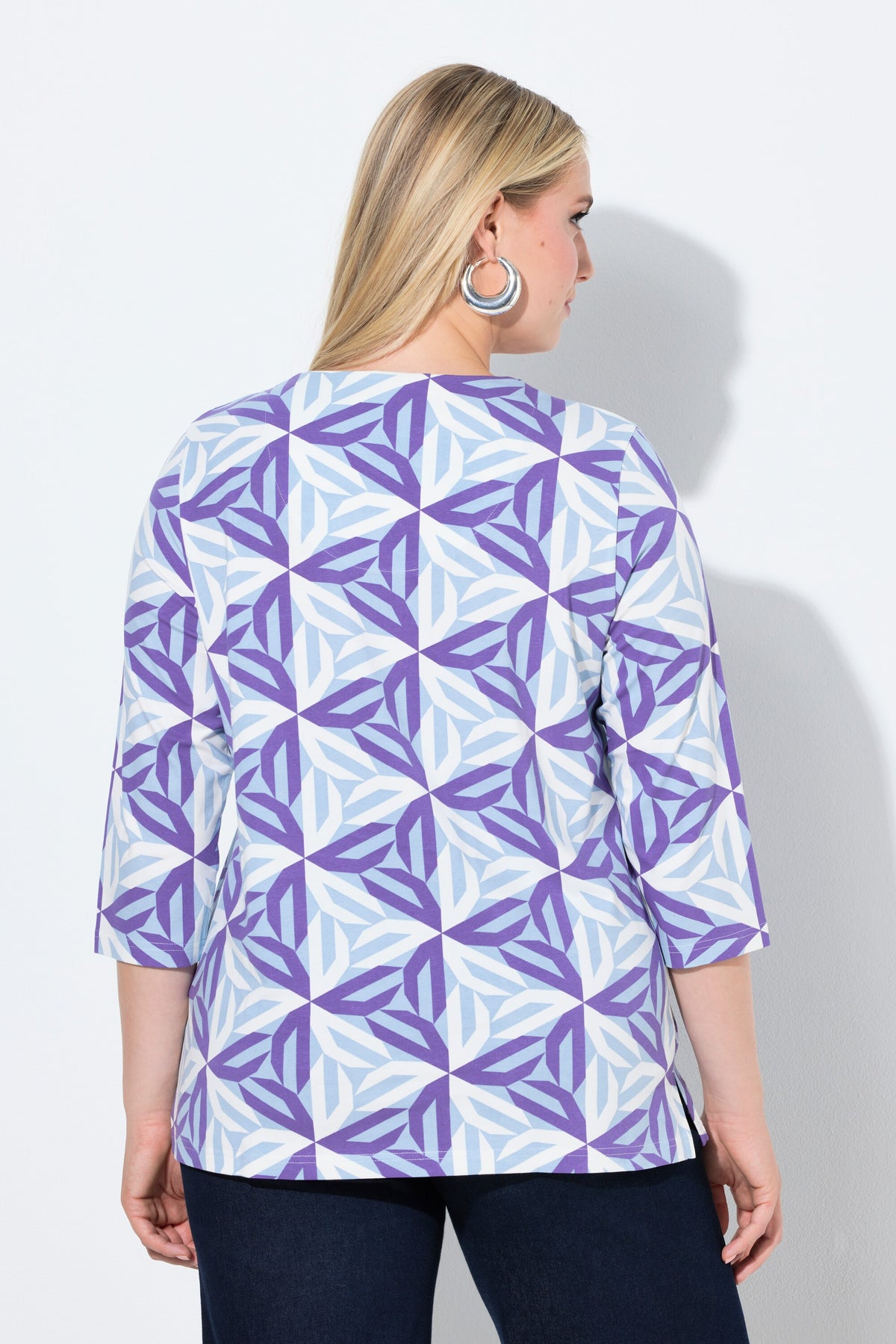 Woman wearing the Ulla Popken Geometric Top in Purple, a purple geometric patterned top with a V neckline, 3/4 length sleeves and an A-line shape against a white background