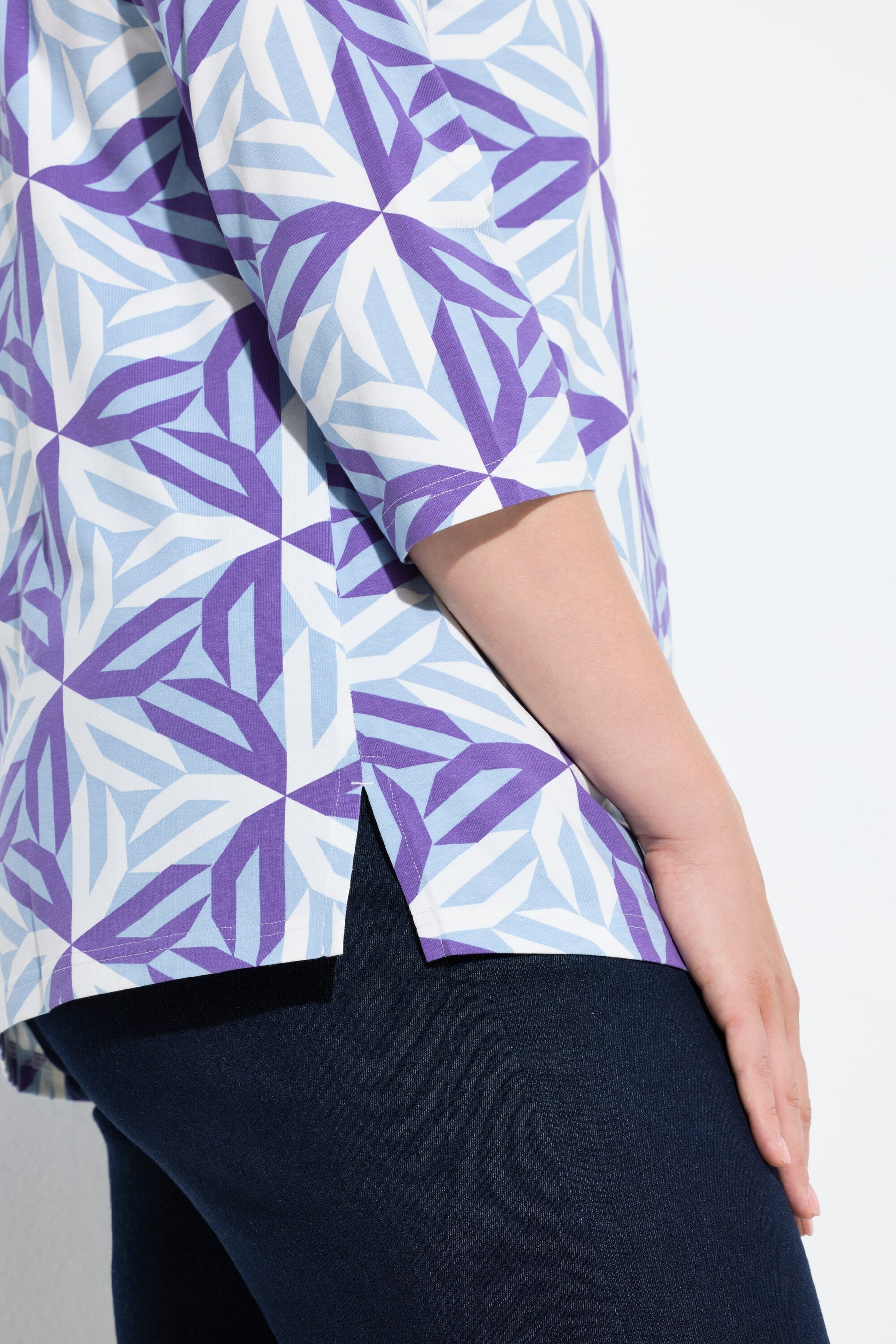 Close-up of a person wearing the Ulla Popken Geometric Top in Purple, a patterned shirt with purple and blue design with small side slits on a white background