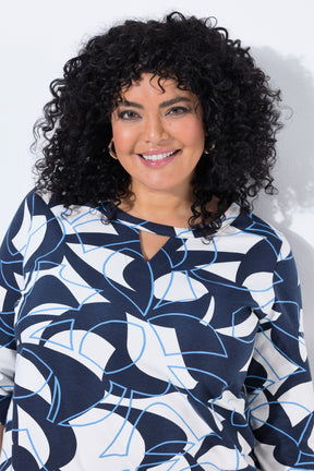 A smiling woman with voluminous curly black hair wearing the Ulla Popken Keyhole Leaf Print Blouse in Navy, a navy, white, and light blue abstract patterned long-sleeve top, photographed against a plain white background.