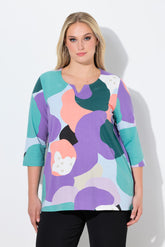Woman wearing the Ulla Popken Multicolor A-Line Top, a colorful abstract patterned top with a tunic neckline, 3/4 length sleeves and an A-line shape against a white background