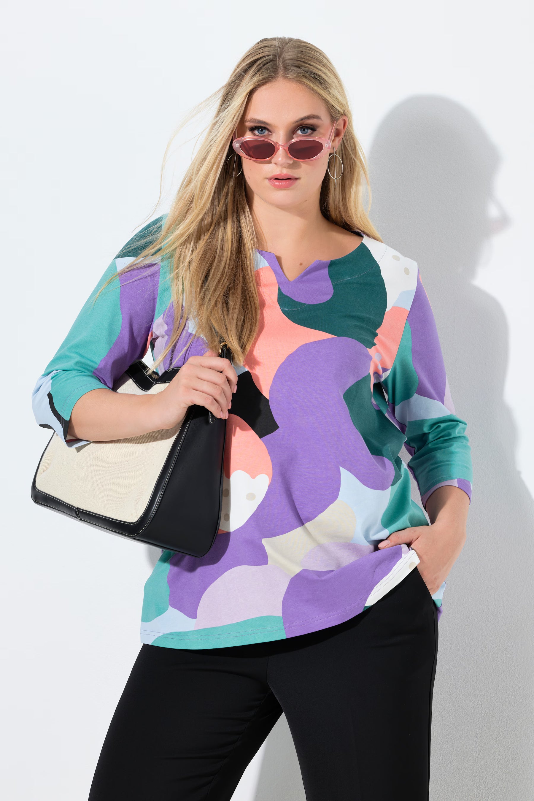 Woman wearing the Ulla Popken Multicolor A-Line Top, a colorful abstract patterned top with a tunic neckline, 3/4 length sleeves and an A-line shape against a white background  