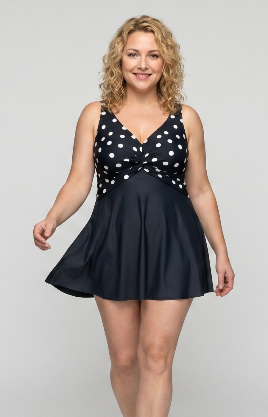 Woman wearing a navy swimsuit with white polka dots on a plain background