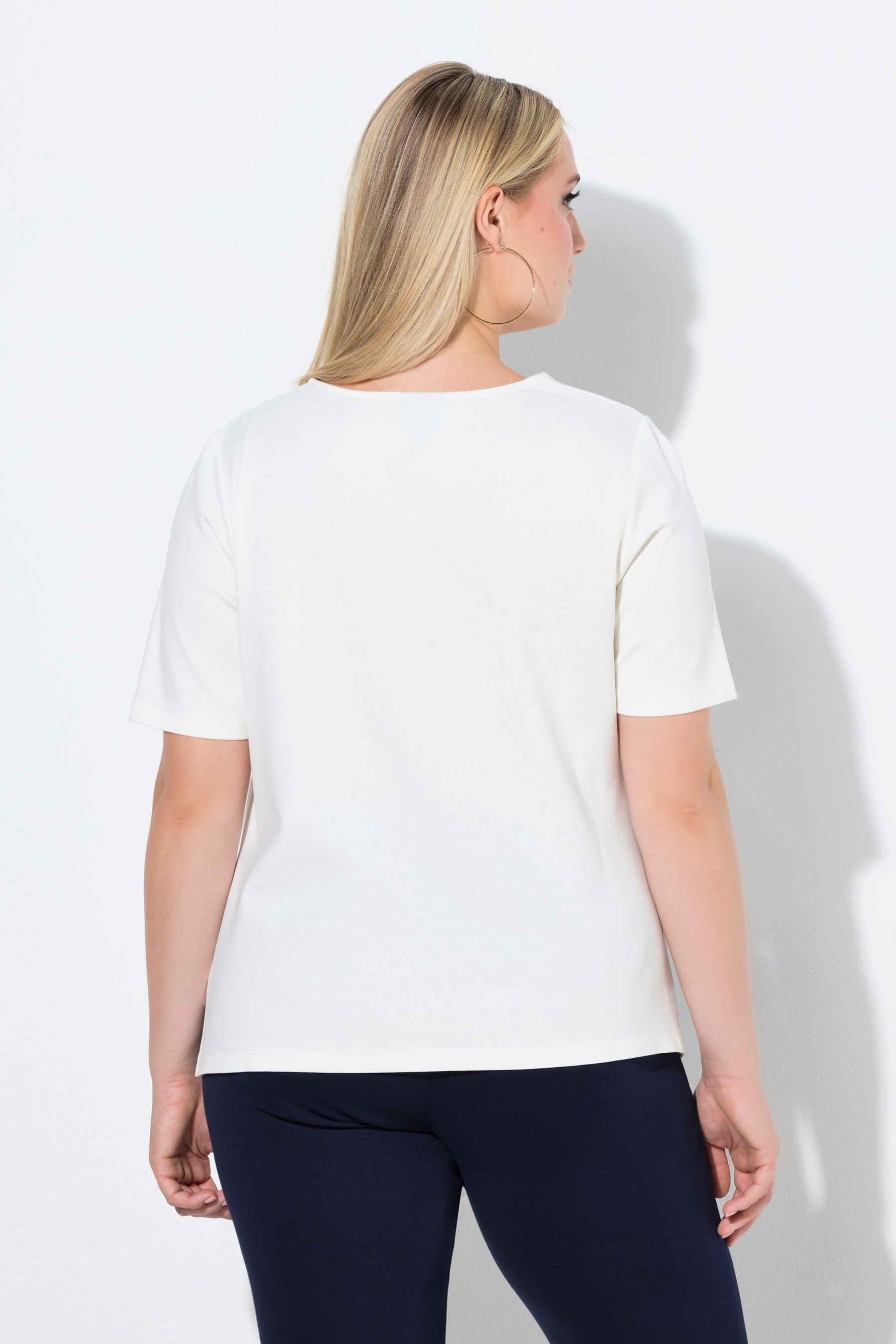 Woman wearing the Ulla Popken Pointed Hem T-Shirt in Off White, a white t-shirt with a round neckline, a pointed hem and draping on the shoulder and side worn with dark pants on a white background