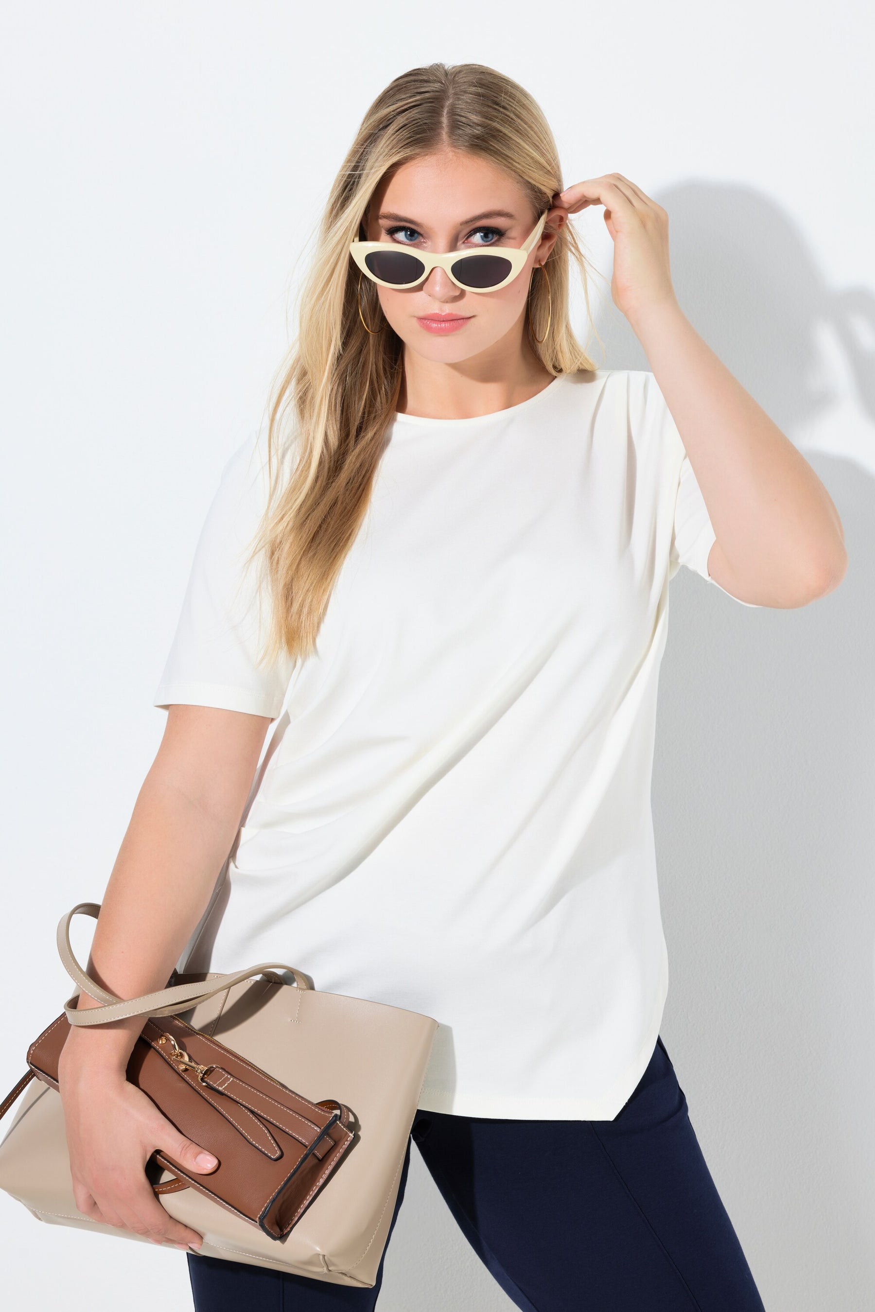 Woman wearing the Ulla Popken Pointed Hem T-Shirt in Off White, a white t-shirt with a round neckline, a pointed hem and draping on the shoulder and side worn with dark pants on a white background