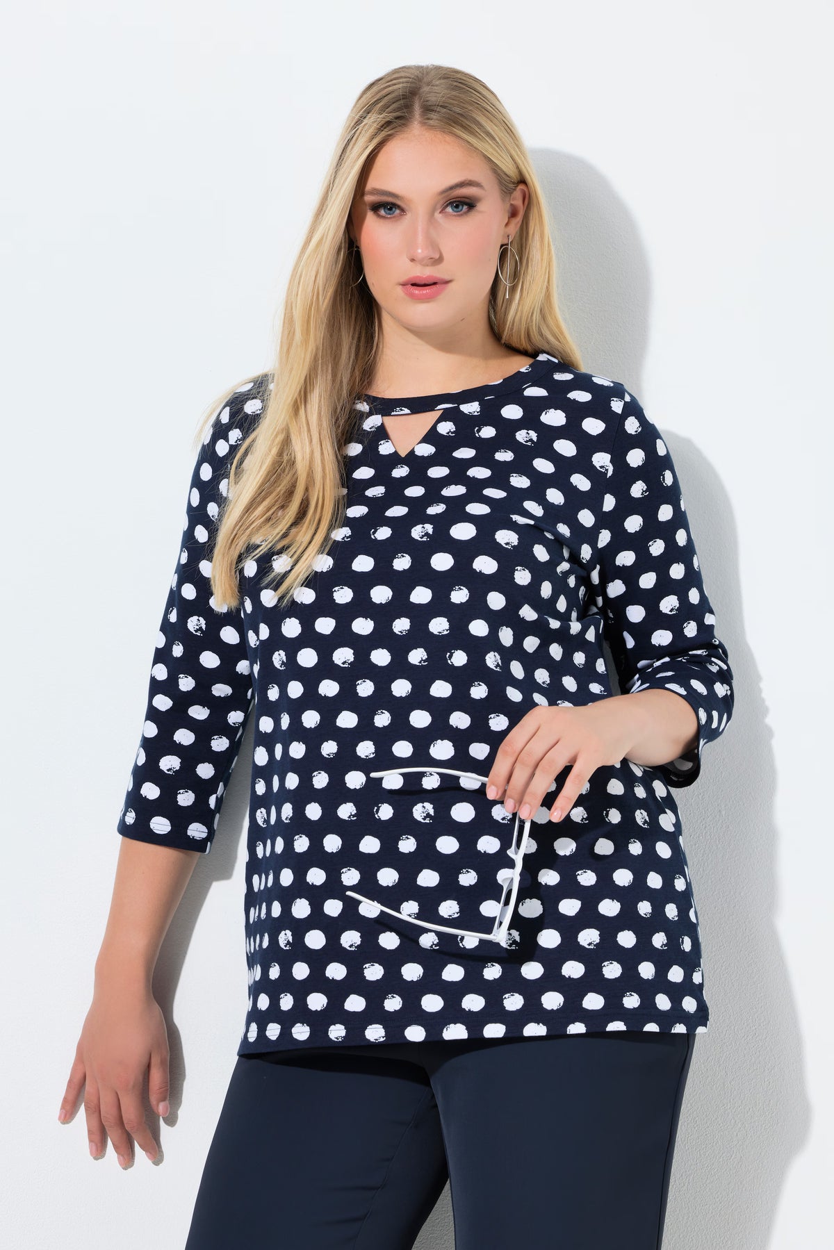 Woman wearing the Ulla Popken Polka Dot Keyhole Top in Navy, a navy blue top with white polka dots against a light background