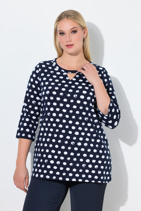 Woman wearing the Ulla Popken Polka Dot Keyhole Top in Navy, a navy blue top with white polka dots with a round neckline with a keyhole cut out and 3/4 length sleeves against a light gray background