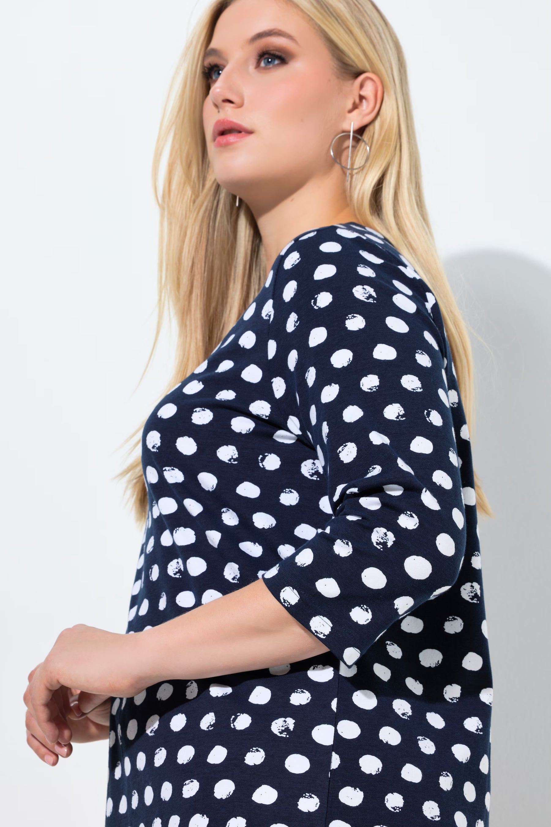 Woman wearing the Ulla Popken Polka Dot Keyhole Top in Navy, a top with 3/4 length sleeves and an A-line shape against a plain background