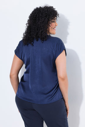 A woman with curly black hair is shown from the back wearing the Ulla Popken Satin Blouse in Navy a short-sleeve navy blue top and matching navy pants against a light gray studio background.