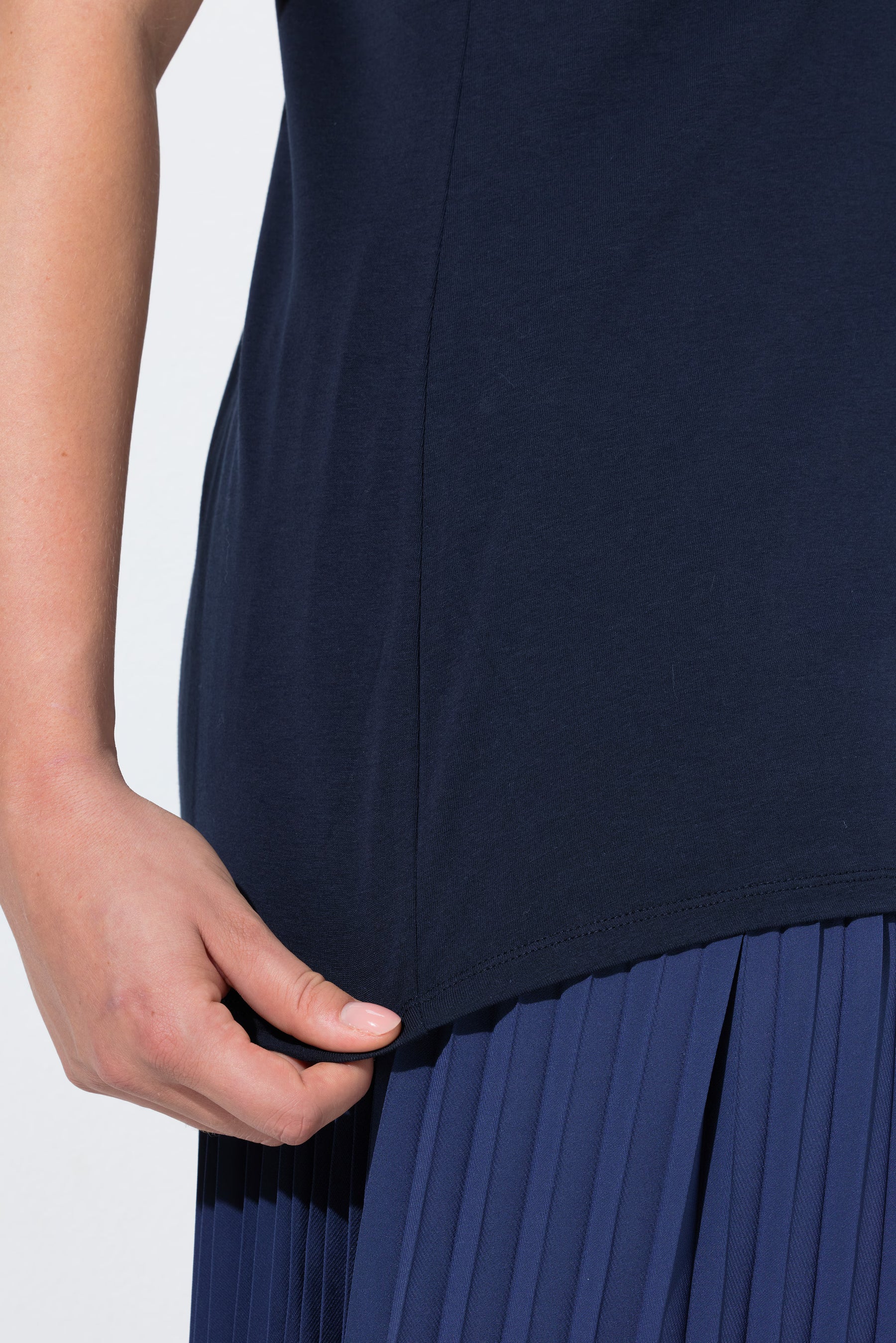 Close up of a woman wearing the Ulla Popken Vest Top in Navy, a navy blue sleeveless top with a round neckline and close fit, worn with a pleated navy skirt